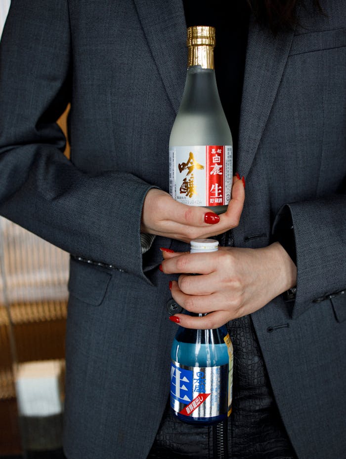 A woman in a suit holds two Japanese sake bottles, showcasing them with elegance.